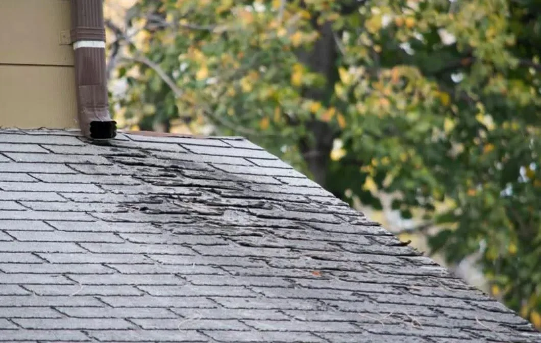 Gray shingles worn and broken up on a roof slope below a downspout that ends on the roof