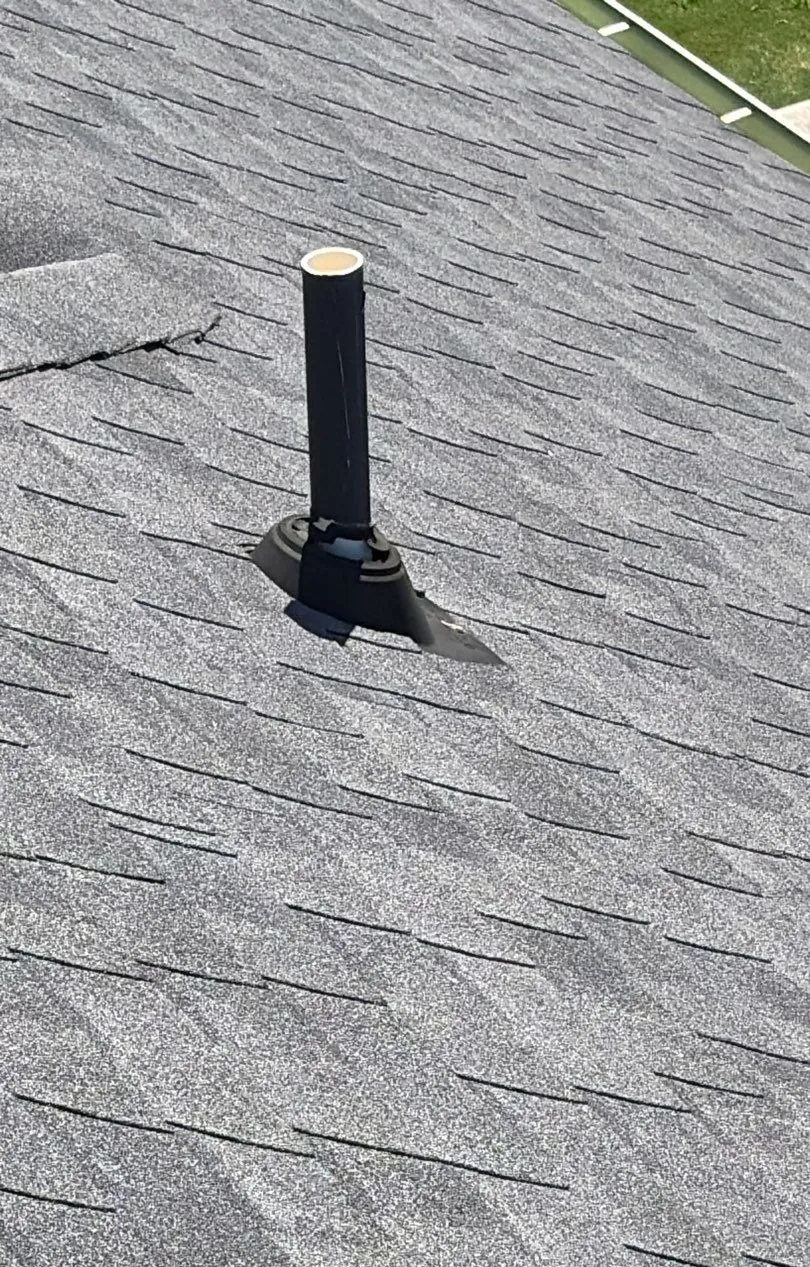 Plumbing vent pipe on a gray shingle roof with a dried-out, cracked rubber pipe boot at its base