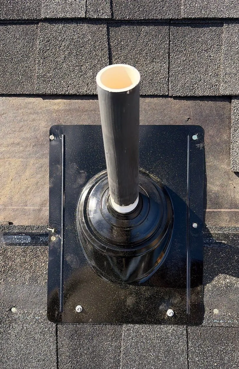 New black pipe boot on a shingle roof with its flange fastened by screws with rubber washers, shingles laid back around it