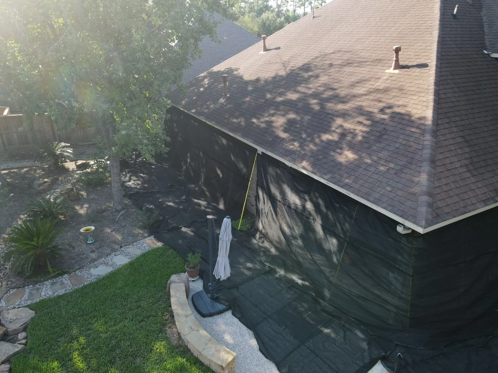Back of a home with black netting hung from the roof edge to the ground and laid over the patio