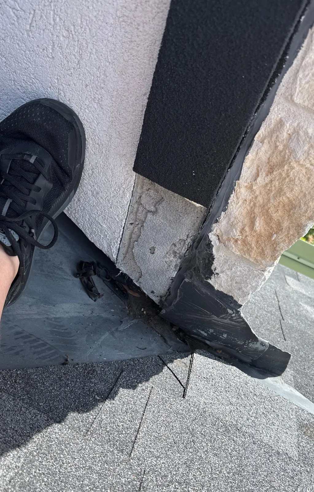 Black tar smeared over torn flashing where a roof meets a stucco and stone wall